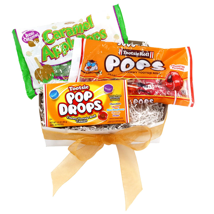 Assorted candy packages including Caramel Apples, Tootsie Pop Drops, and Tootsie Roll Pop in a box with a yellow ribbon on a white background.